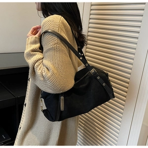 Detail of black suede shoulder bag featuring metallic eyelets and golden hardware on strap