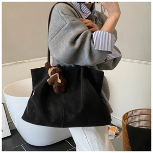 Detailed view of large black suede tote bag with a brown teddy bear charm on shoulder