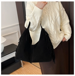 Detail of a black suede hobo bag with fringe accents worn with a casual winter outfit