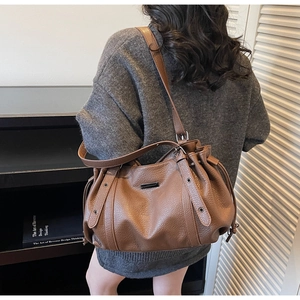 Detail view of brown lychee grain leather tote bag with drawstring on a female model