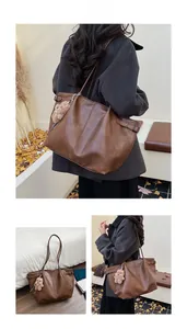Detail of a brown leather tote bag with a metal buckle and a cute plush bear charm
