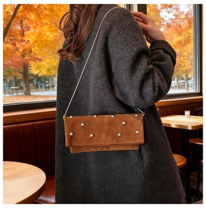 Close-up of caramel suede shoulder bag featuring metal studs and a fine chain strap