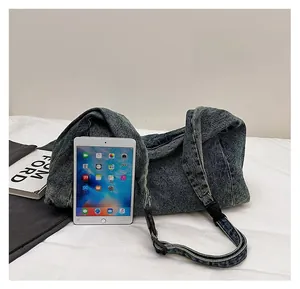 Spacious denim shoulder bag shown next to a tablet and books for size reference