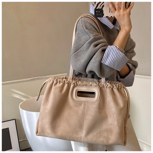 Sac fourre-tout en suédine beige avec cordon de serrage porté par un mannequin en intérieur