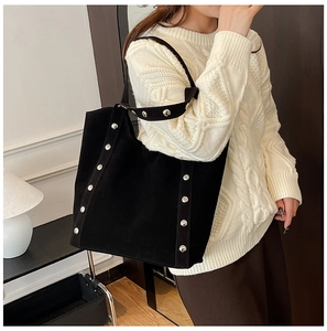 Close-up of black suede tote bag featuring silver rivet studs on a model's shoulder