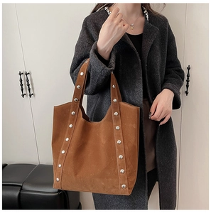 Brown suede tote bag with silver rivets shown on shoulder of model in grey wool coat