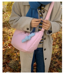 Dettaglio borsa trapuntata rosa con ciondolo nodo blu su cappotto beige in autunno