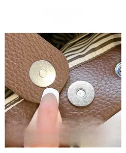 Detail der silbernen Magnetschnalle an brauner Lederhandtasche mit Streifenfutter