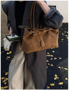 Detail of a brown suede tote bag with decorative buckle and strap in a chic street setting