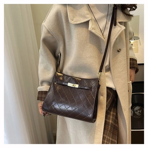 Close-up of quilted dark brown shoulder bag with golden lock on a wool coat outfit