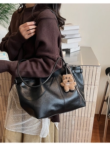 Detail of black tote bag with smooth leather texture and cute brown teddy bear charm