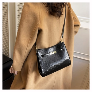 Detail view of black quilted leather underarm bag worn with a camel wool coat on shoulder