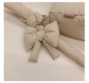Détail d'un pendentif nœud en tissu crème avec une chaîne à billes argentée sur un sac