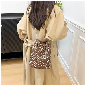 Braune Nieten-Beuteltasche mit Silberkette und Perle, getragen zu einem modischen Trenchcoat