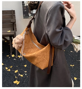 Close-up of yellow pleated shoulder bag with brown leather strap and plush bear charm