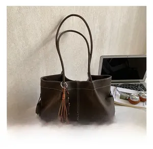 Detail view of coffee brown suede tote bag with contrast stitching and bear charm accessory