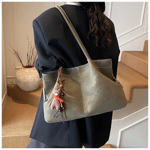 Detail of olive green suede tote bag featuring white contrast stitching and bear charm