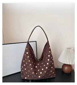 Detail of vintage brown suede hobo bag with gold rivet studs on a black surface