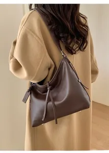 Modèle portant un sac bandoulière en cuir marron foncé sur un manteau en laine de chameau