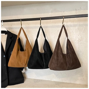 Detailed view of three suede tote bags in brown and black with white decorative stitching