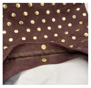 Detailed close-up of dark brown suede bag with gold rivet studs and magnetic snap closure