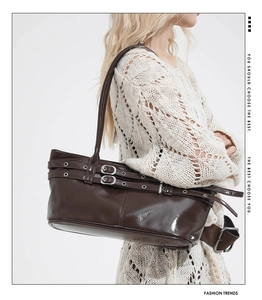 Detail of dark brown glossy underarm bag with decorative silver buckle straps and eyelets