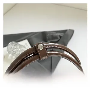 Detail of dark brown glossy leather handles with a polished silver snap button closure