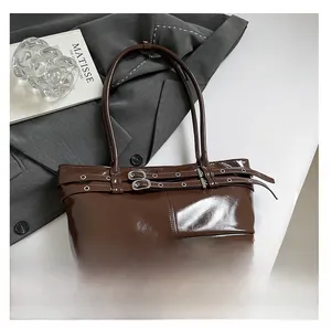 Detail of dark brown glossy baguette bag with double belt buckles and silver eyelets