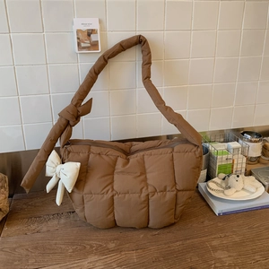 Détail d'un sac à main matelassé marron foncé avec bandoulière rembourrée et nœud blanc