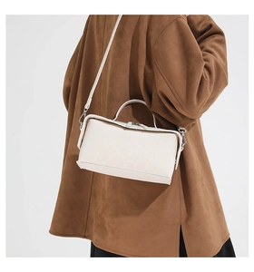 Detail view of a cream leather rectangular shoulder bag worn with a brown winter coat