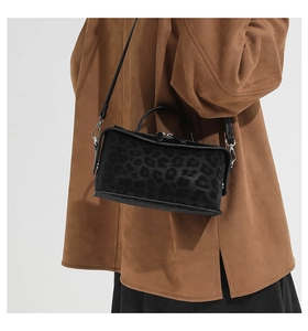 Detailed close-up of leopard print suede handbag with top handle and leather strap