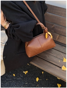 Sac Boston en cuir marron avec boucle dorée présenté sur un banc de parc extérieur