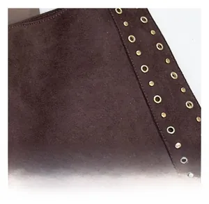 Detailed view of dark brown suede fabric with metallic studs and eyelets on shoulder bag