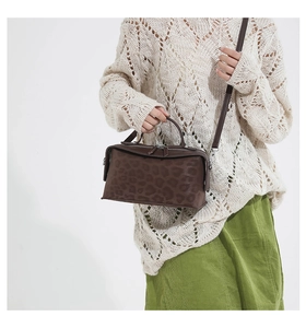 Detail of a dark brown leopard print crossbody bag worn by a model in a white studio