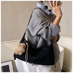 Mirror selfie showing a black pleated shoulder bag with a teddy bear charm and tassels