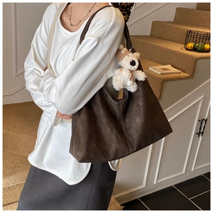 Macro view of dark brown suede tote bag with white stitching and plush bear charm