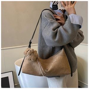 Close-up of brown crinkled texture handbag with cute plush bear charm on shoulder strap