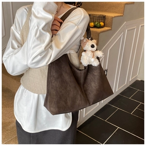 Detail of dark brown matte shoulder bag with white contrast stitching and plush bear charm