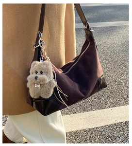 Detail of suede and leather patchwork dumpling bag with a plush dog charm on shoulder