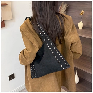 Detail of black suede shoulder bag with metallic eyelets and rivets on a model's shoulder
