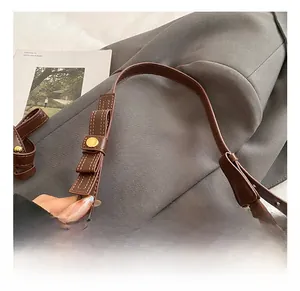 Detail of dark brown leather handbag handle with gold round buckle and fine stitching