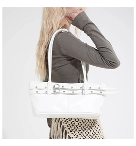 Detail view of white shoulder bag with decorative belts, eyelets and metal buckles