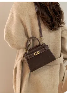 Detail of dark brown suede handbag with white contrast stitching and golden oval twist lock