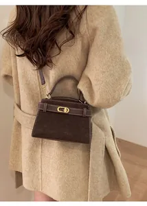 Detail of dark brown suede crossbody bag featuring gold lock and white contrast stitching