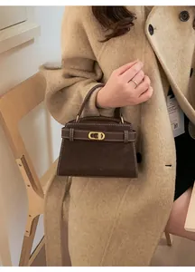 Close-up of brown suede handbag featuring white contrast stitching and a gold metal clasp
