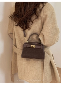 Deep brown retro suede mini bag with gold lock shown cross-body on a beige coat