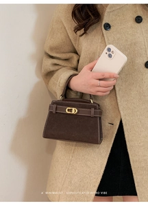 Detail of dark brown suede handbag with golden buckle worn with a beige wool coat