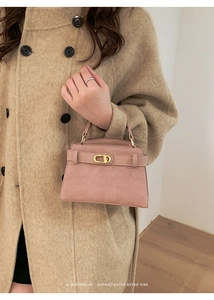 Detail view of pink matte leather handbag with gold clasp on minimalist wool coat