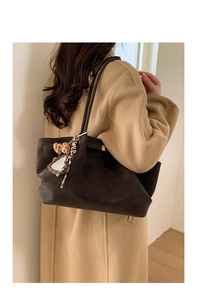 Detail of dark brown suede tote bag featuring a plush leopard print ball charm on a model