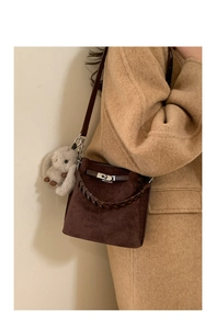 Detail of suede bucket bag with metal clasp and plush bunny charm on a wool coat